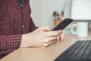 Home office concept: Man is typing on his black mobile phone