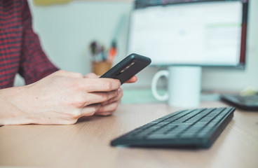Home office concept: Man is typing on his black mobile phone