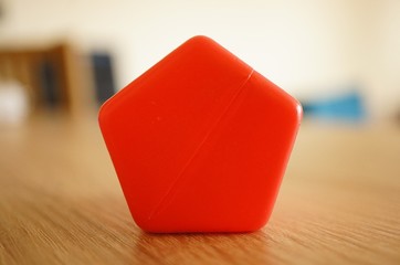 Shallow focus shot of a red pentagon shape plastic toy block with a blurred background