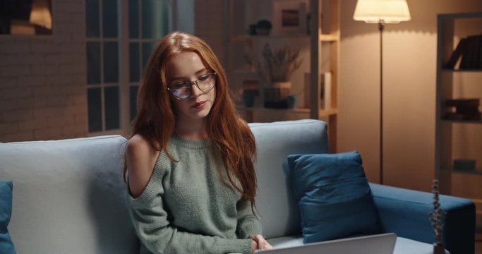 Pretty caucasian young redhead girl using a laptop, remote manager talking and working on a project, high school or university student preparing for a test, concentrating on information 4k footage