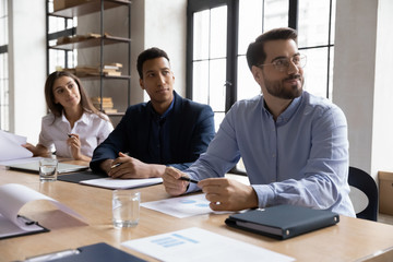 Concentrated multiracial businesspeople sit at desk in boardroom listen to coach or presenter...