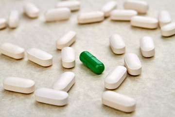Pile of white medical pills. Special green pill amoung white ones.