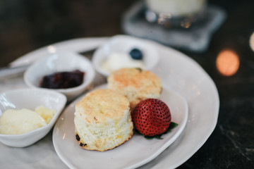 Butter scones served with jam and clotted cream with strawberries on white plate.Breakfast, Traditional English Afternoon Tea, Scones with Clotted Cream and Strawberry Jam, Selective Focus