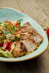 Warm salad with grilled turkey, tomatoes, pistachios, lettuce in a blue bowl on a wooden background. Healthy diet