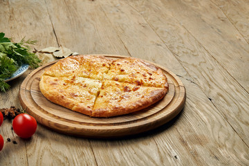 Close up view on tasty traditional Khachapuri - closed baked pie stuffed with melted salt cheese (suluguni) or meat on wooden tray. Traditional georgian food