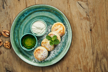 Homemade cheesecakes or Syrniki with jam, fresh fruits and sour cream in ceramic plate. Ukrainian cuisine. Breakfast food. Wooden background