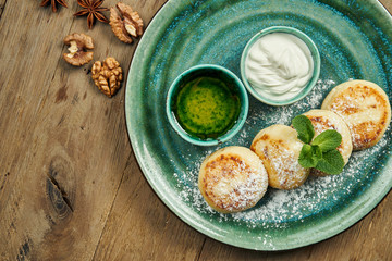 Homemade cheesecakes or Syrniki with jam, fresh fruits and sour cream in ceramic plate. Ukrainian cuisine. Breakfast food. Wooden background