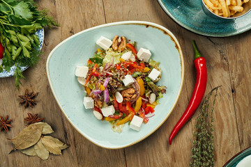 Classic Greek salad with tomatoes, onions, cucumber, feta cheese and black olives in white plate on a wooden background. Close up view. Food flat lay