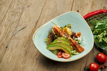 Tasty salad with grilled salmon, avocado, lettuce in a blue bowl on a wooden background. Seafood salad
