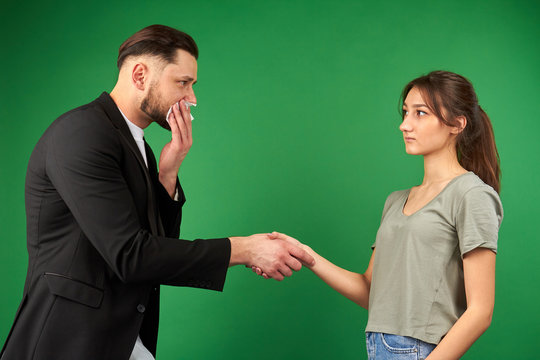 Man and a woman handshaking on green background. Sick businessman with handkerchief tries not to cough.