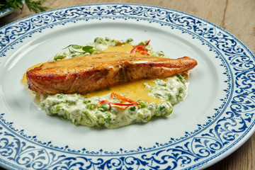 Delicious grilled salmon steak filet with peas in a creamy sauce in a white plate on a wooden background. Tasty seafood