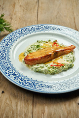 Delicious grilled salmon steak filet with peas in a creamy sauce in a white plate on a wooden background. Tasty seafood