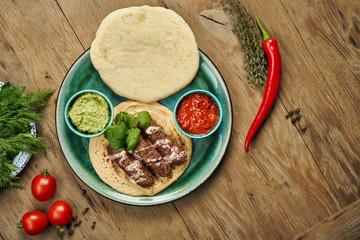 Appetizing rolls of Lyulya kebab - cooked over a lamb minced meat with a side dish of hummus with pita and salsa on ceramic plate. Vertical, wooden background, Eastern cuisine
