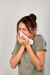 Young woman with handkerchief having cold. Girl blowing nose or sneezing in tissue on white...