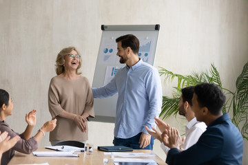 Smiling young businessman greeting excited middle-aged female employee at office meeting with...
