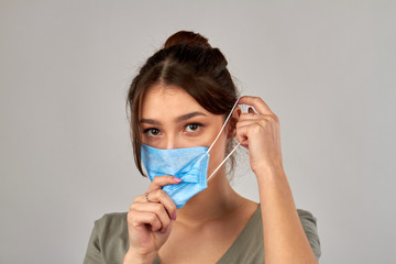 Portrait of young girl putting on medical mask. Protection from coronavirus. Isolated on grey background.