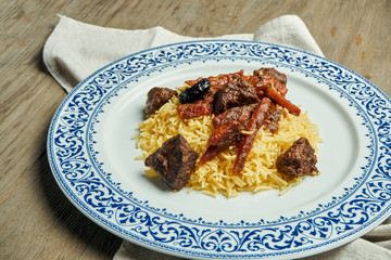 Light, diet pilaf with beef and carrots on a white plate on a wooden background. Top view with copy space for text. Traditional oriental cuisine