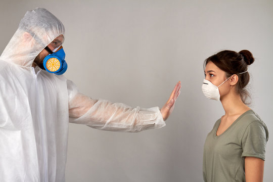 Stay away from me! Don't come closer. Man in protective clothing covid19 showing stop gesture to a girl isolated on grey background.
