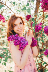 Handsome brown hair girl in light dress near the lilac tree smiles