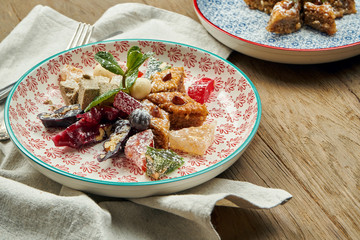 Classic Turkish baklava with pistachios and honey in a ceramic plate on a wooden background. Turkish pastries and sweets. Close up