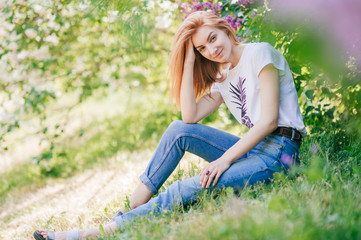 Naklejka na ściany i meble Portrait of emotional red-hair girl sits in a lilac garden
