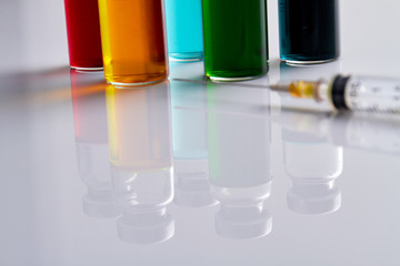Medicine vials reflecting on white surface. Macro shot of syringe and bottles.