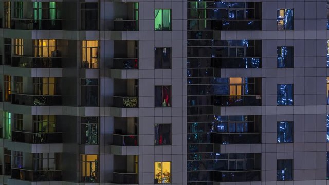 Rows of glowing windows with people in the interior of apartment building at night. Modern skyscraper from glass and concrete. Concept for business and modern life. Zoom in