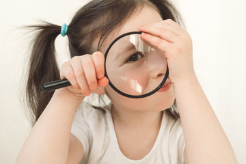 Little girl plays a detective. A child examines something through a magnifying glass. A girl with...