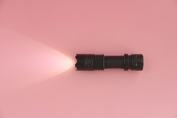 The black turned on electric manual lamp lies on a pink background. Light from a lantern on the...