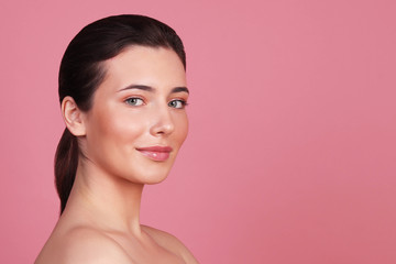 Portrait of a young brunette woman with clean skin on a pink background, natural female appearance