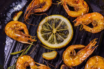 Roasted shrimps with lemon slice, garlic and rosemary in a cast iron pan. Top view