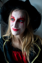 Portrait of a young girl with blond hair as a witch with bright make-up and leaking lipstick mysteriously looks to the side