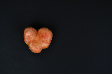 Heart-shaped potato on a black background. Symbol of love. Organic food.