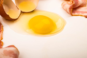 A broken chicken egg and sliced bacon on a white background. Close up.
