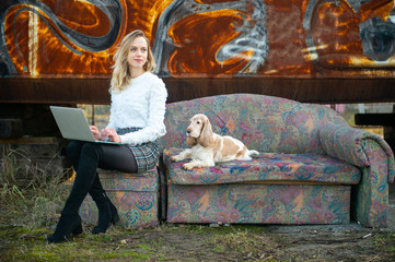 Cheerful caucasian young freelancer girl sitting on old couch outdoor over rusty graffiti wall on...