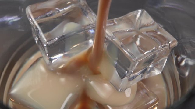 Irish cream liqueur is poured into a glass with ice cubes. Macro shot. Alcoholic drinks at the bar.