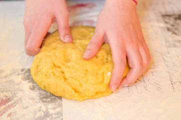 Female hands knead the dough for a sweet cake on a table sprinkled with flour. Making shortcrust pastry at home in the kitchen. Selective focus.