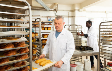 Naklejka na ściany i meble Baker putting tray with bakery goods on trolley