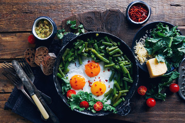Pan of fresh fried eggs with tomatoes, green beans, bread, spices and herbs on rustic wooden background