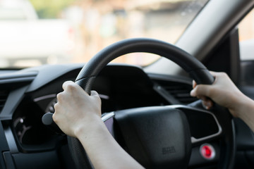 Female hands on the steering wheel of a car while driving. Against the background, the windshield and road,Close-up of a woman's hand driving a car