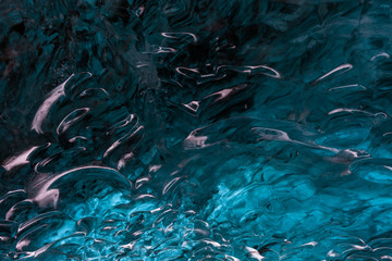 The surface of the ice cave from the inside. Texture of turquoise ice with black volcanic sand inside. Natural blue ice surface close up