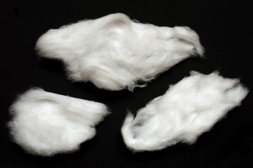 Clouds made of cotton wool isolated on black background. Three clumps of white fluffy cotton wool isolated on a black background close-up. Set of white lumps of cotton wool on a black background.