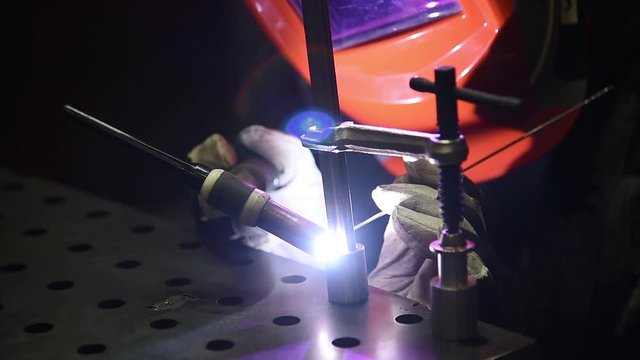 A welder produces custom clamps for working on a steel welding table