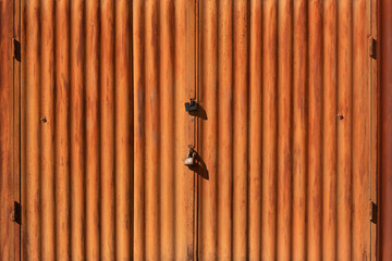 A fragment of an old garage door made of corrugated sheet metal painted orange with two padlocks