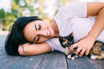 Beautiful young girl lies on floor with little kitten and smiles