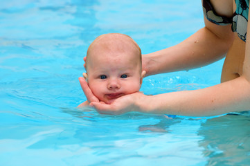 Fototapeta na wymiar Baby swimming in pool with mother's help