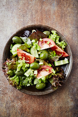 Healthy salad with green olives, cucumber and tomatoes. Rustic stone background. Top view. 