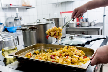 Chef cooks fried potatoes with pieces of meat in a restaurant kitchen