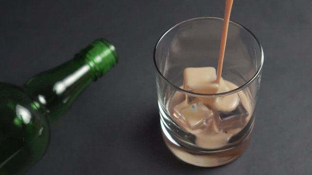 Irish cream liqueur is poured into a glass with ice cubes. Empty green bottle. Alcoholic drinks at the bar.