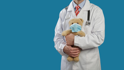 Pediatrician medical doctor with a stethoscope holds a teddy bear in a medical mask.